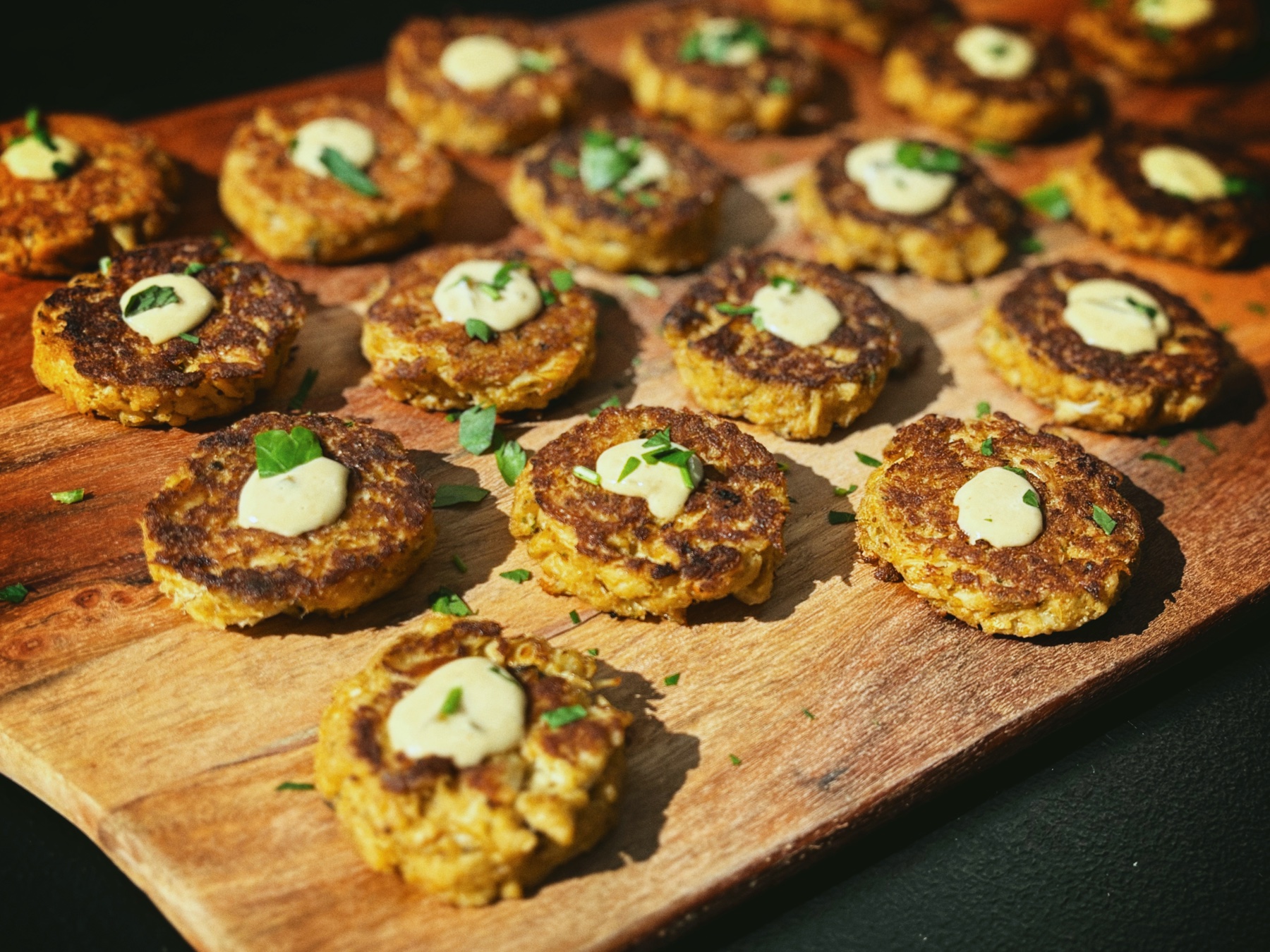 Crab cake bites with sauce and herbs arranged on a wooden serving board