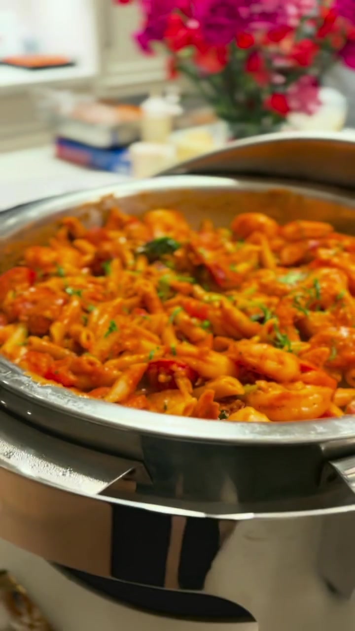Pasta presented in a polished serving dish with pink flowers nearby
