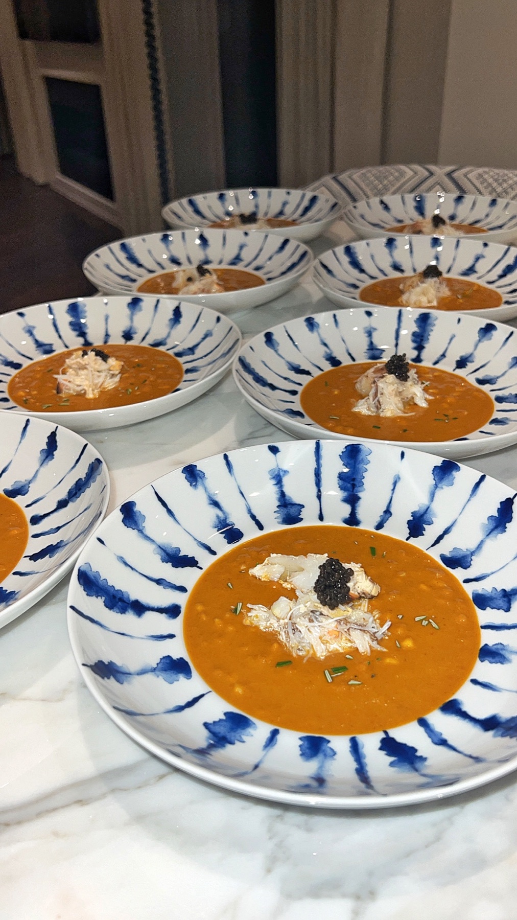 Plated soup garnished with seafood and caviar in blue-and-white bowls